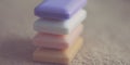Stack of four bars of soap different colors on a brown towel.