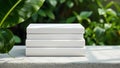 A stack of four blank white books rests on a textured concrete surface beside a large green leaf Royalty Free Stock Photo