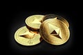 Stack of four golden Ethereum coins laying on the black background
