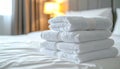 Stack of four neatly folded white towels on a made bed with crisp white sheets and pillows in a hotel room Royalty Free Stock Photo