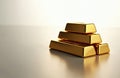 Stack of four shiny gold bars on clean light surface. Bars vary in size, indicating different weights. Selective focus highlights Royalty Free Stock Photo