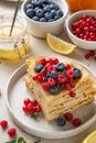 Stack of French crepes or Russian blini on white plate. Thin pancakes with raspberries, blueberries, currant, lemon jam and tea. Royalty Free Stock Photo