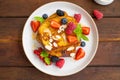 A stack of French toast on a plate with fresh berries, almond petals and honey on a dark wooden background. Delicious breakfast.