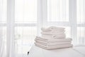 Stack of fresh white bath towels on bed sheet in modern hotel bedroom interior with window on background, copy space. Royalty Free Stock Photo