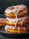 Stack of freshly baked golden donuts generously coated with sweet white icing dripping over the edges on a dark ceramic plate Royalty Free Stock Photo