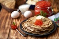 A stack of freshly prepared pancakes with red caviar, on a black plate on a wooden background, next to a spoon with red caviar Royalty Free Stock Photo