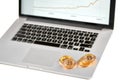 Stack of golden bitcoins placed on silver laptop with blurred financial chart on its screen.