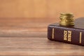 Stack of golden coins on top of holy bible book on a wooden background Royalty Free Stock Photo