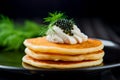 Stack of golden pancakes crowned with a dollop of cream and a generous spoonful of black caviar