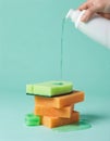 Stack of green, orange sponges with liquid detergent poured onto top sponge. Small green sponge sits beside stack, with spilled Royalty Free Stock Photo