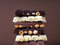 Stack of half chocolate bars with hazelnuts - milk chocolate, dark chocolate and white chocolate on brown background Royalty Free Stock Photo