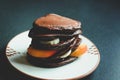 Stack of homemade chocolate pancakes with honey, bananas, peach served on a beige plate over black stone texture background