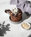 Stack of homemade chocolate pancakes with melted chocolate, ground almond and marshmallow, light background. Direct sunlight and