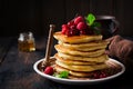 Stack of homemade little pancakes with honey, fresh raspberries and red currants on an old wooden background.