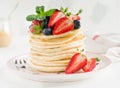 Stack of homemade little pancakes with honey, fresh strawberries and sauce on light wooden background.