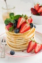 Stack of homemade little pancakes with honey, fresh strawberries and sauce on light wooden background.