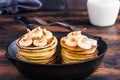 Stack of homemade pancakes with banana, maple syrup and walnuts in black cast iron skillet.