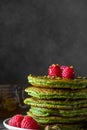 Stack of homemade pancakes with matcha tea, fresh raspberries, pistachios and honey on black background Royalty Free Stock Photo