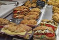 Stack of hot dogs in baguette buns covered with melted cheese on display at a local sandwich shop in Nice, France