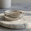 A stack of intricately designed silver bangles sits on a round, white marble surface. Royalty Free Stock Photo