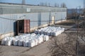 Stack of large bags next to a concealed industrial warehouse outdoors. Cargo handling and storage