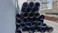 Stack of large black industrial corrugated plastic pipes at construction site, residential buildings in background Royalty Free Stock Photo