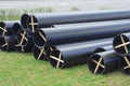 Stack of large black pipes for water mains with blue stripes, rests on a grassy field Royalty Free Stock Photo