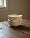 A stack of light cream-colored ceramic bowls sitting on a dark brown wooden table Royalty Free Stock Photo