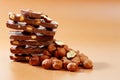 Stack of milk chocolate pieces and hazelnuts on brown background