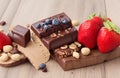 Stack of milk and dark chocolate with nuts, caramel and fruits and berries on wooden background