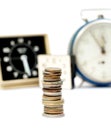 Stack of mixed old rusty coins in front of alarm clock in the blur background. Time is Money concept Royalty Free Stock Photo