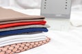 A stack of multicolored clothes close up with the white modern electrical iron of background - ironing, laundry and housework Royalty Free Stock Photo