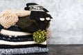 A stack of neatly folded knitted winter scarves, hats with pompons and gloves on gray background. Season of warm clothes