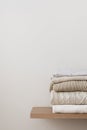 A stack of neatly folded warm knitwear, wool on a wooden shelf and a beige background.