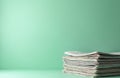 Stack of newspapers rests on mint green surface against solid mint green background. Clean, organised pile of print media Royalty Free Stock Photo