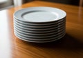 A stack of nine white ceramic plates is neatly arranged on a polished wooden table. The plates are Royalty Free Stock Photo