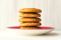 Stack oatmeal cookies on red plate on white wooden table on light wall background