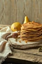 A stack of oatmeal pancakes on a light-colored wooden table, surrounded by a pair of pears in the distance, sea buckthorn berries