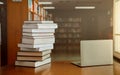 Stack of old books and laptop computer on desk in library background. Educational technology concept