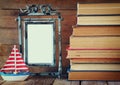 Stack of old books next to decorative sailing boat and blank frame wooden table. vintage filtered image Royalty Free Stock Photo