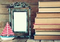 Stack of old books next to decorative sailing boat and blank frame wooden table. vintage filtered image Royalty Free Stock Photo