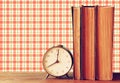 Stack of old books and old clock over wooden table and retro style wallpaper Royalty Free Stock Photo