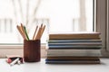 A stack of old books and several different colored pencils lie on the windowsill, a box of crayons lies on the side Royalty Free Stock Photo