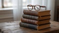 A stack of four antique books rests on a rustic wooden table, topped with a pair of tortoiseshell glasses Royalty Free Stock Photo