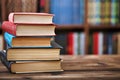 A stack of old paper books on a wooden table. Bookshelves in the background. Blurred background
