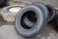 Stack of old used tires of different sizes and types in abandoned scrap yard.