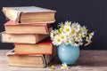 A stack of old vintage books lying on a wooden shelf with a bouquet of daisies in a blue vase. Country still life. Royalty Free Stock Photo