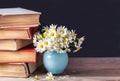 A stack of old vintage books lying on a wooden shelf with a bouquet of daisies in a blue vase. Country still life. Royalty Free Stock Photo