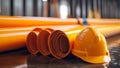 A stack of orange conduit pipes at a construction site has a yellow hard hat resting upon it Royalty Free Stock Photo