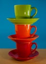 Stack of orange, green, red cups in saucers stand on a wooden table on a blue background Royalty Free Stock Photo